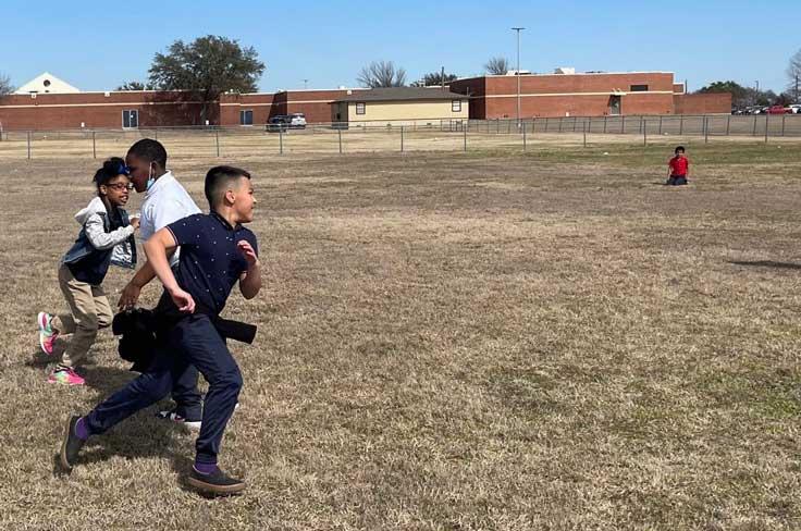 Boys running in open field with school fencing and portable in the background